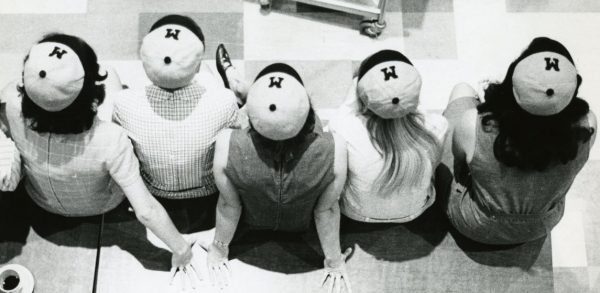 Image of five young women facing away from the viewer, with hats on with the letter M visible.